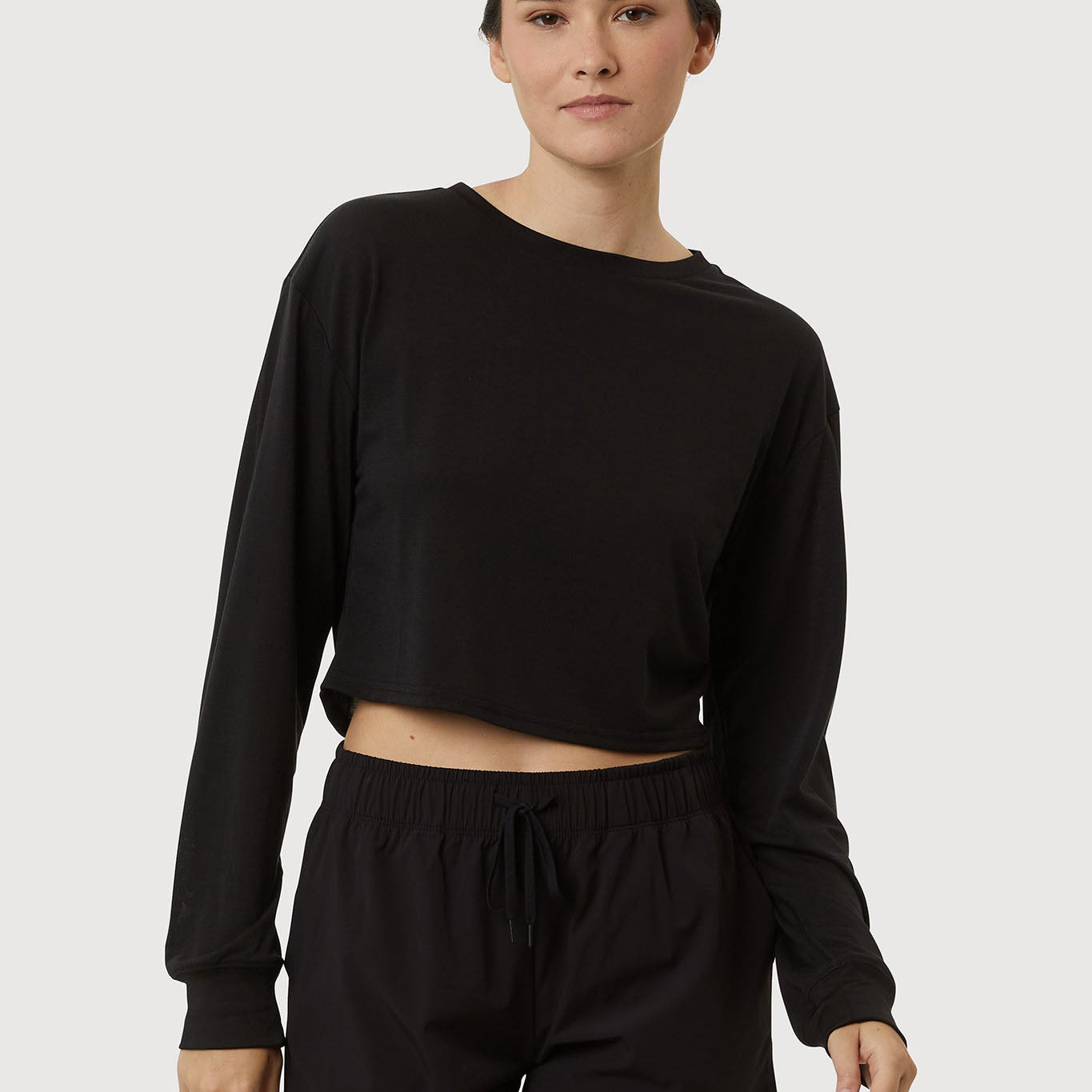 Person wearing a black long-sleeve top and black shorts on a white background