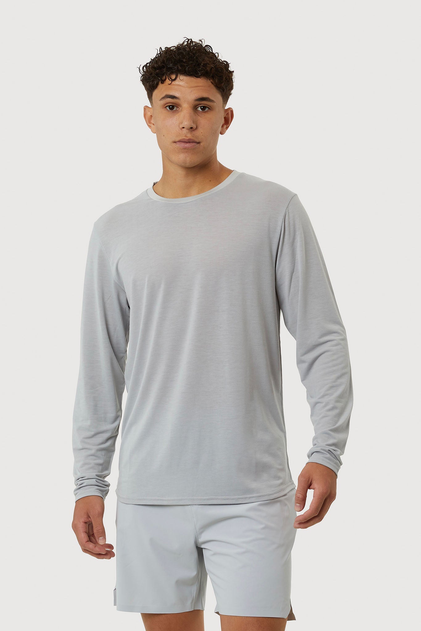 Man wearing a light gray long-sleeve shirt and shorts on a white background