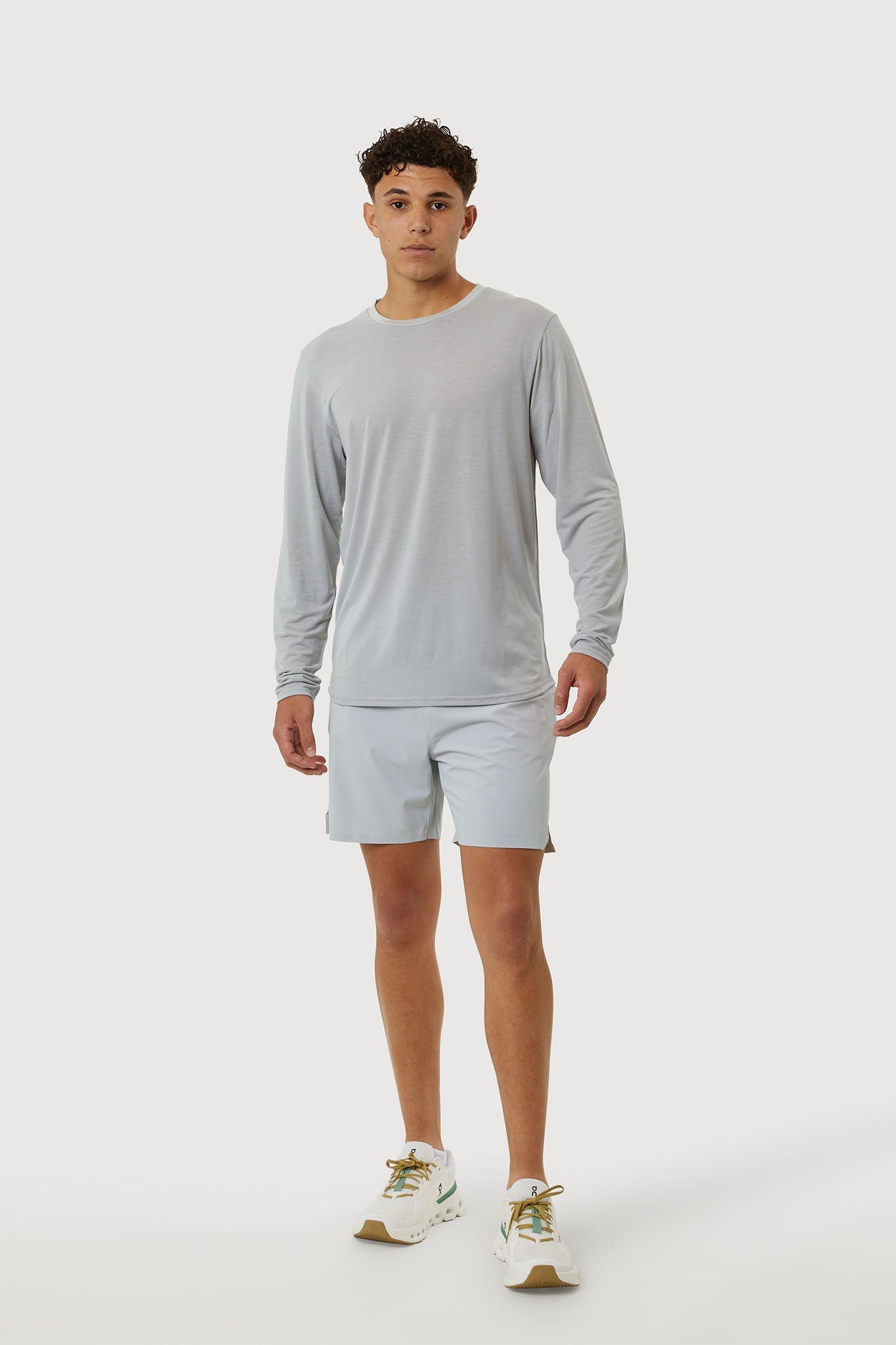 Person wearing a gray long-sleeve shirt and light gray shorts on a white background