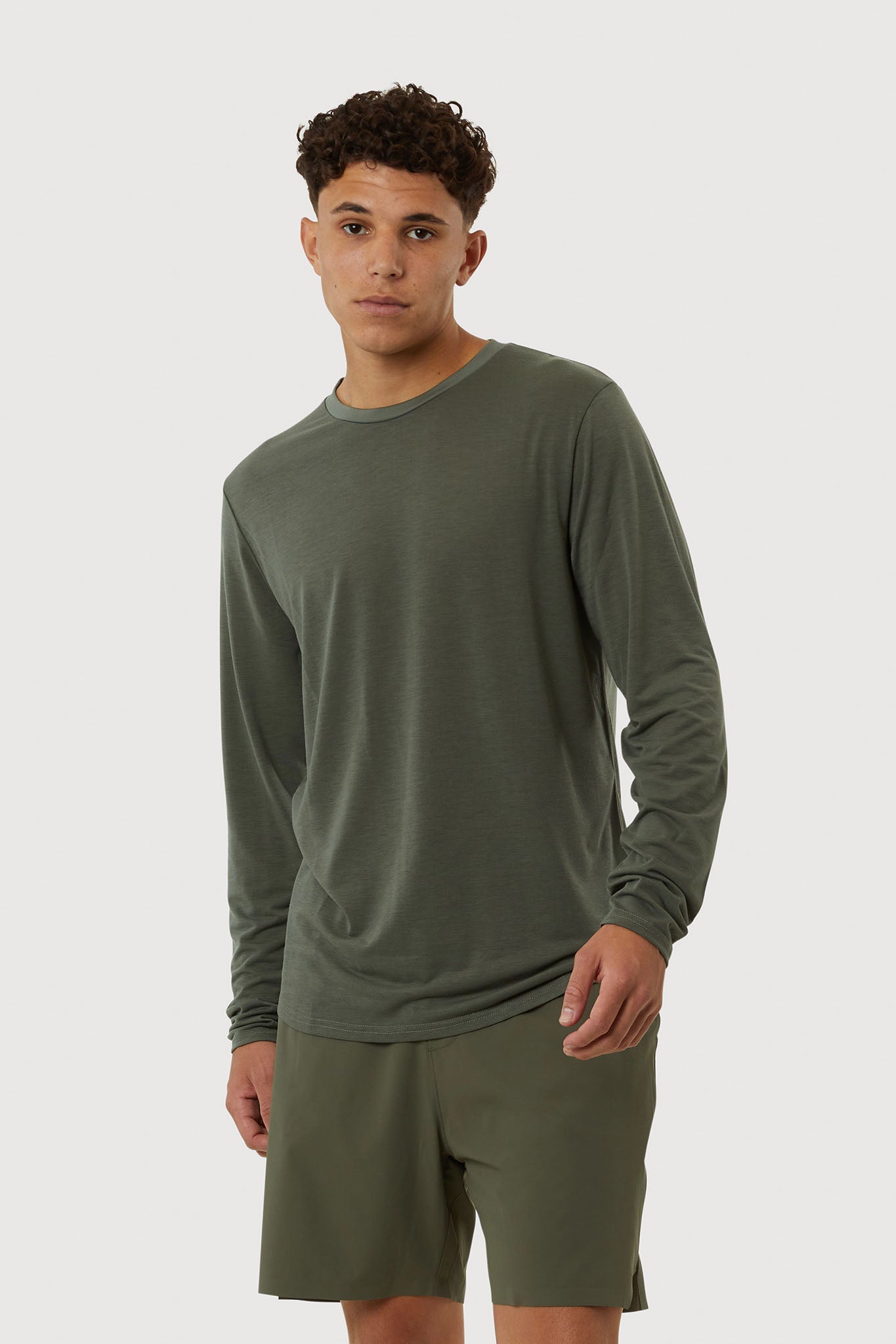 Man wearing a green long-sleeve shirt and shorts on a white background