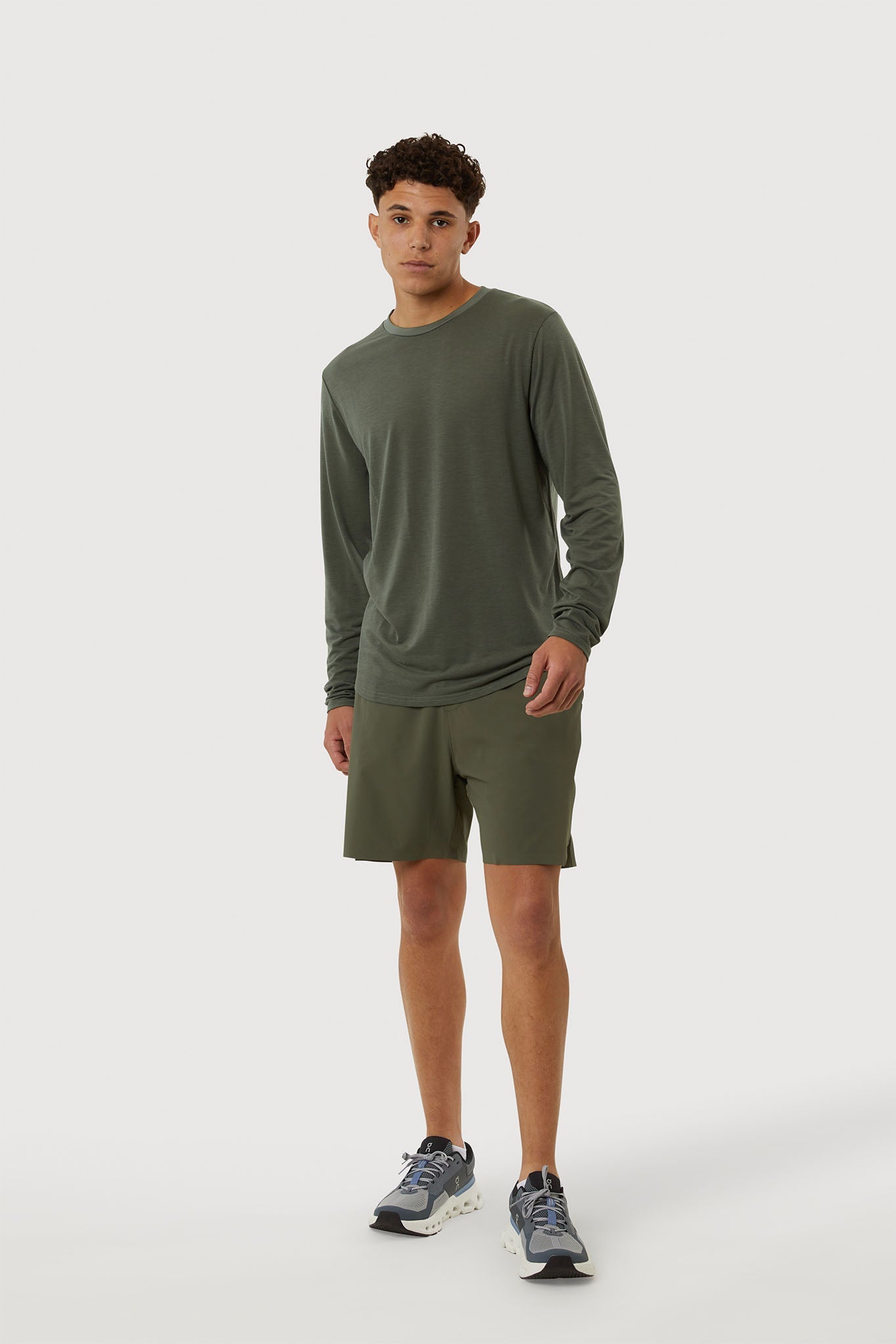 Man wearing a green long-sleeve shirt and shorts on a white background