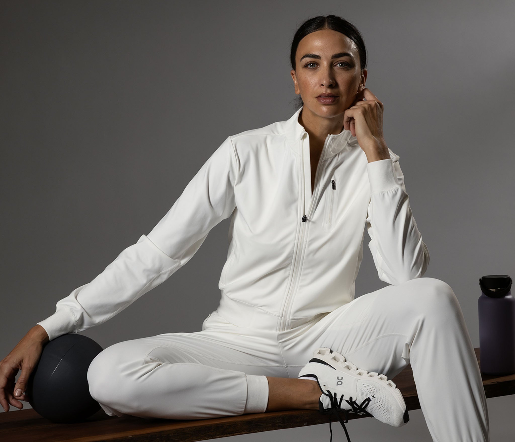 Woman in a white tracksuit sitting on a wooden bench with a gray background