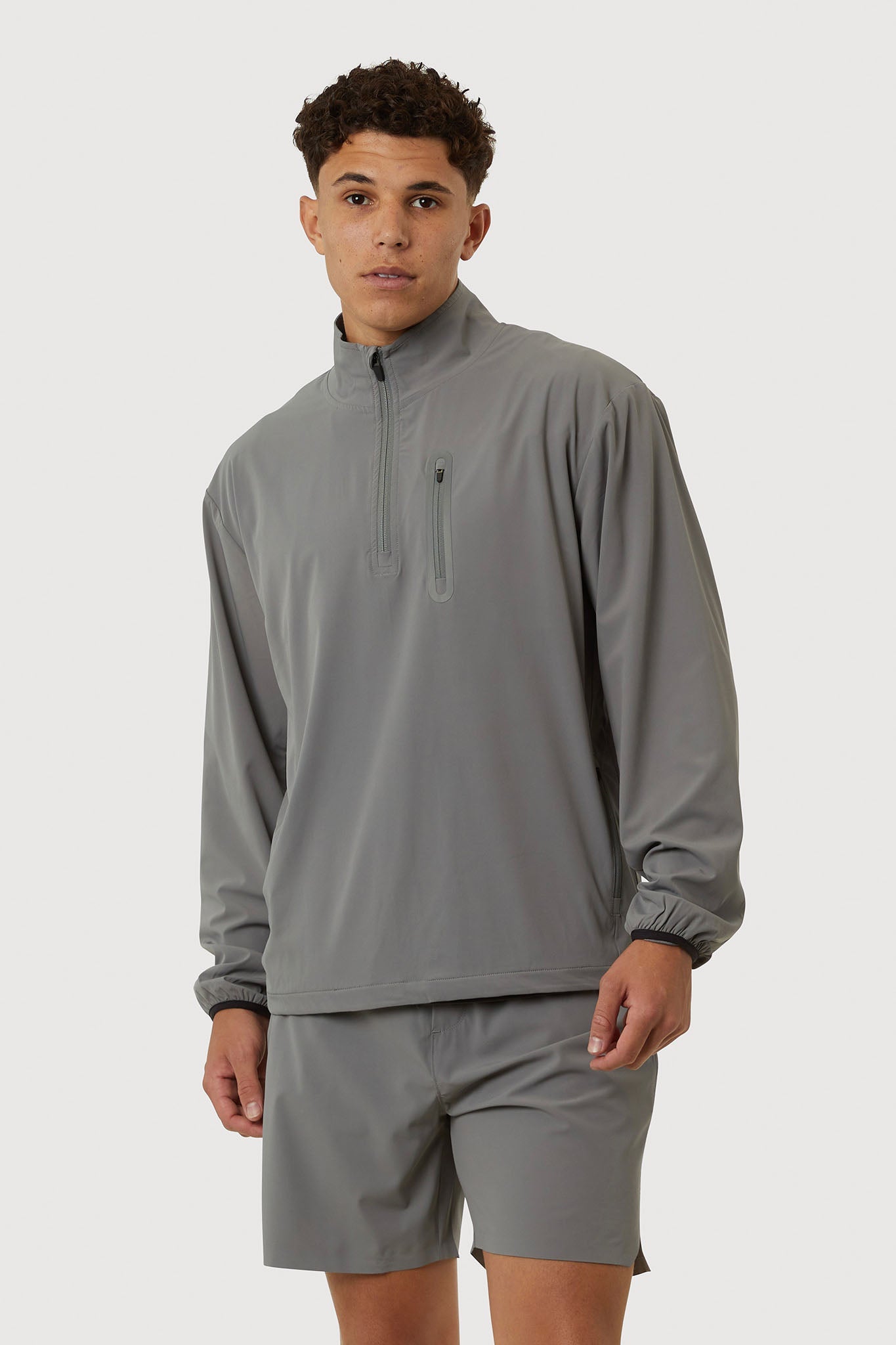 Man wearing a gray quarter-zip pullover and shorts on a white background