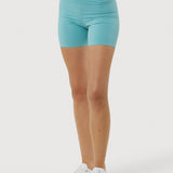 Person wearing turquoise shorts and white sneakers on a white background