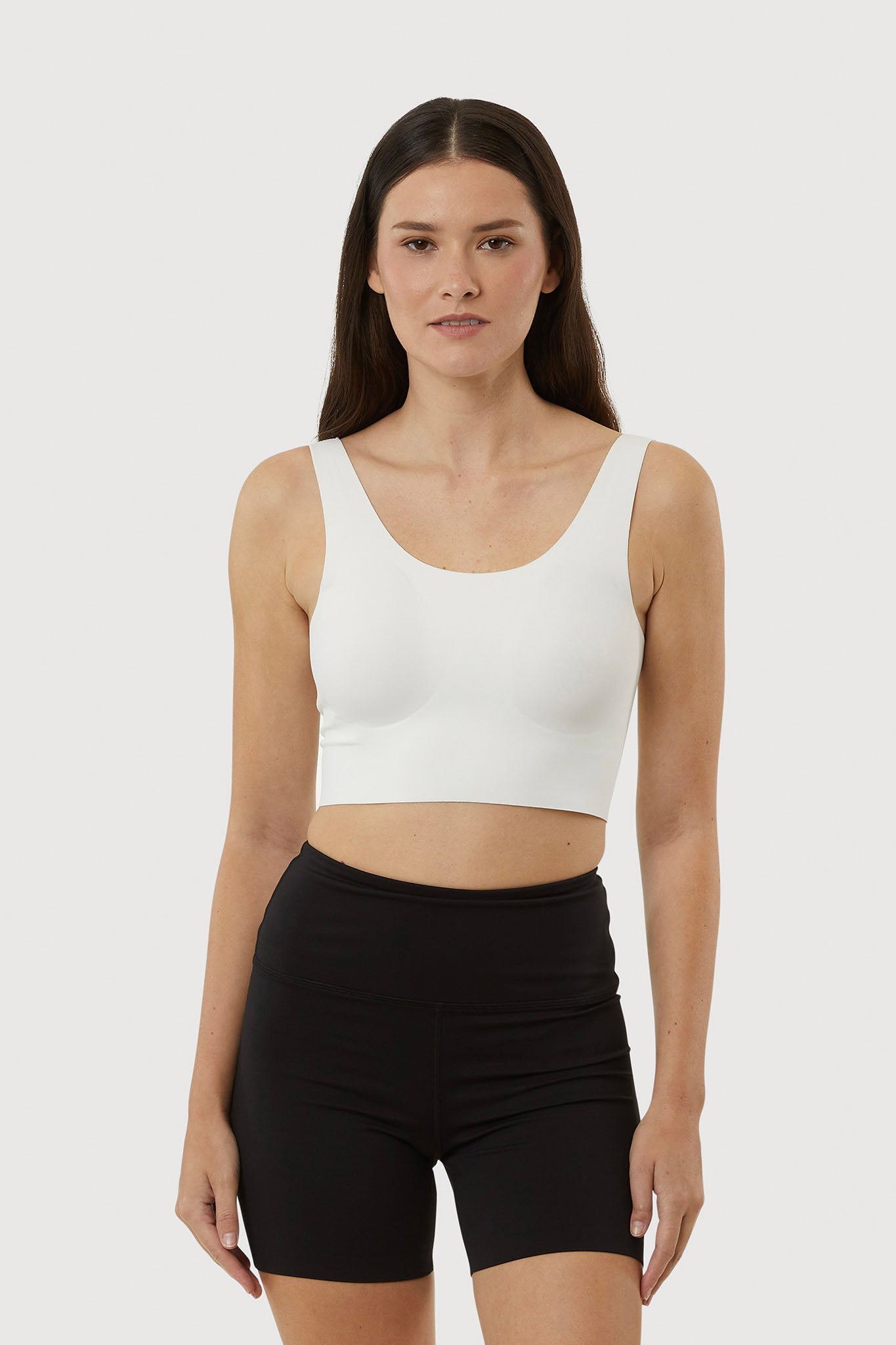 Woman wearing a white tank top and black shorts on a plain background