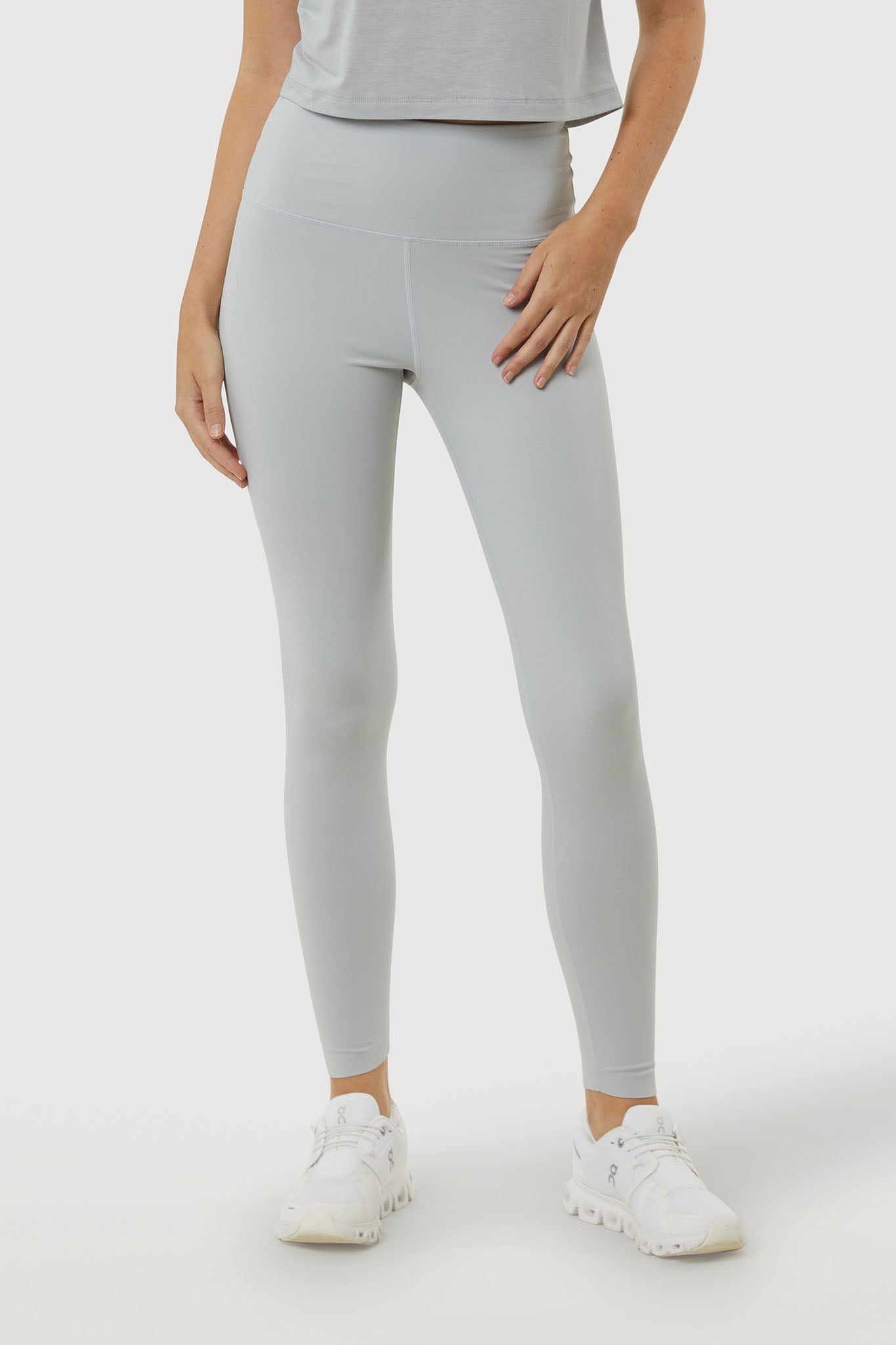 Person wearing light gray leggings and white sneakers on a plain background