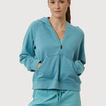 Woman wearing a teal tracksuit on a light gray background