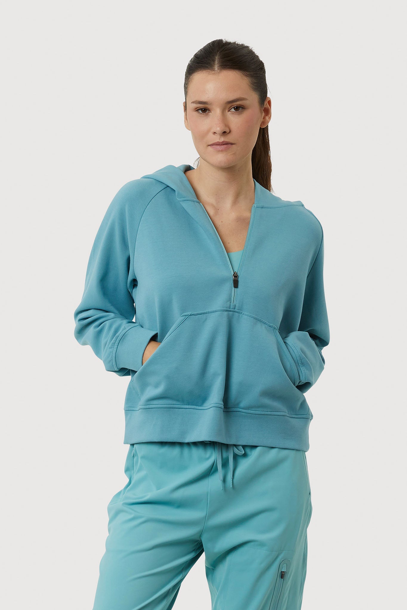 Woman wearing a teal tracksuit on a light gray background