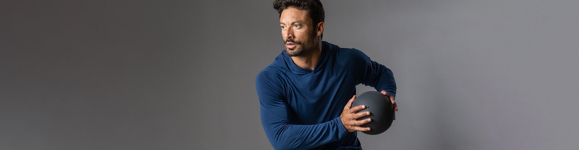Man in a blue sweater holding a rugby ball against a gray background