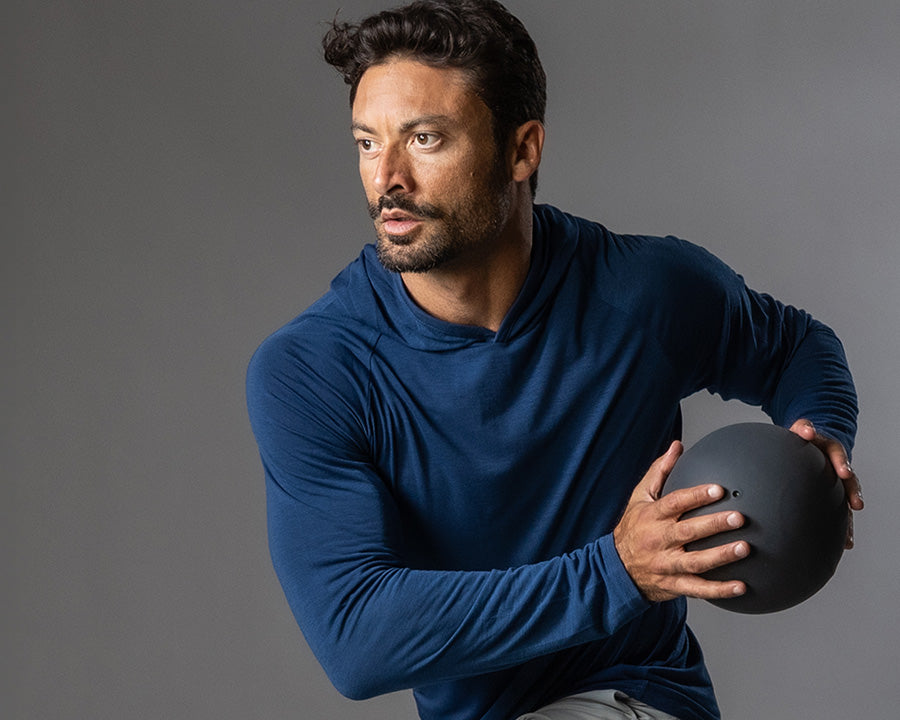 Man in blue long-sleeve shirt holding a black helmet against a gray background
