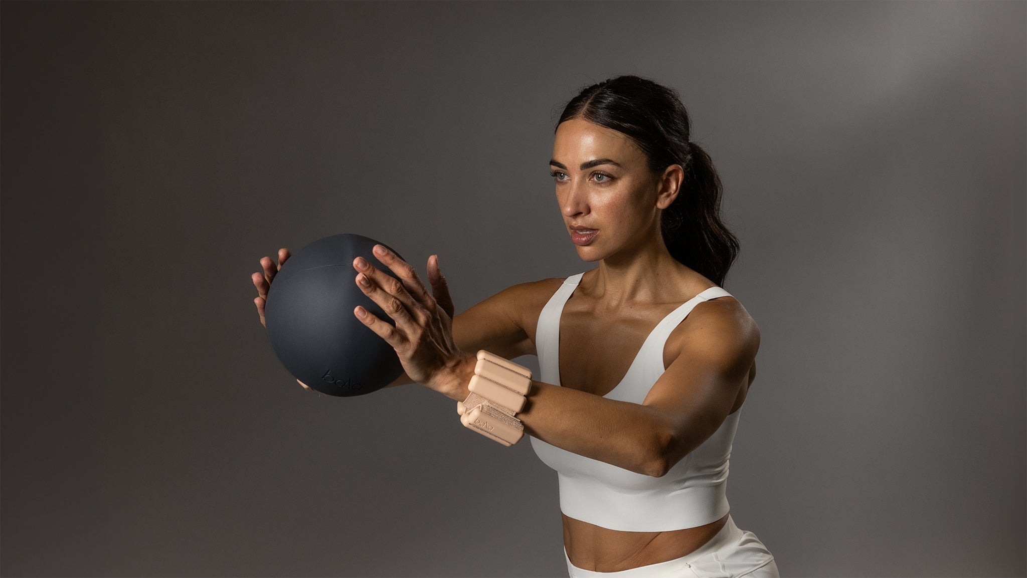 Woman exercising with a medicine ball against a gray background