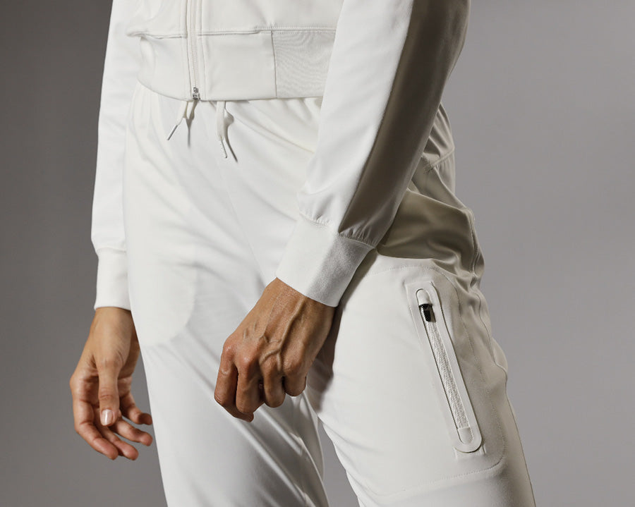 Person wearing a white tracksuit with zippers on a gray background