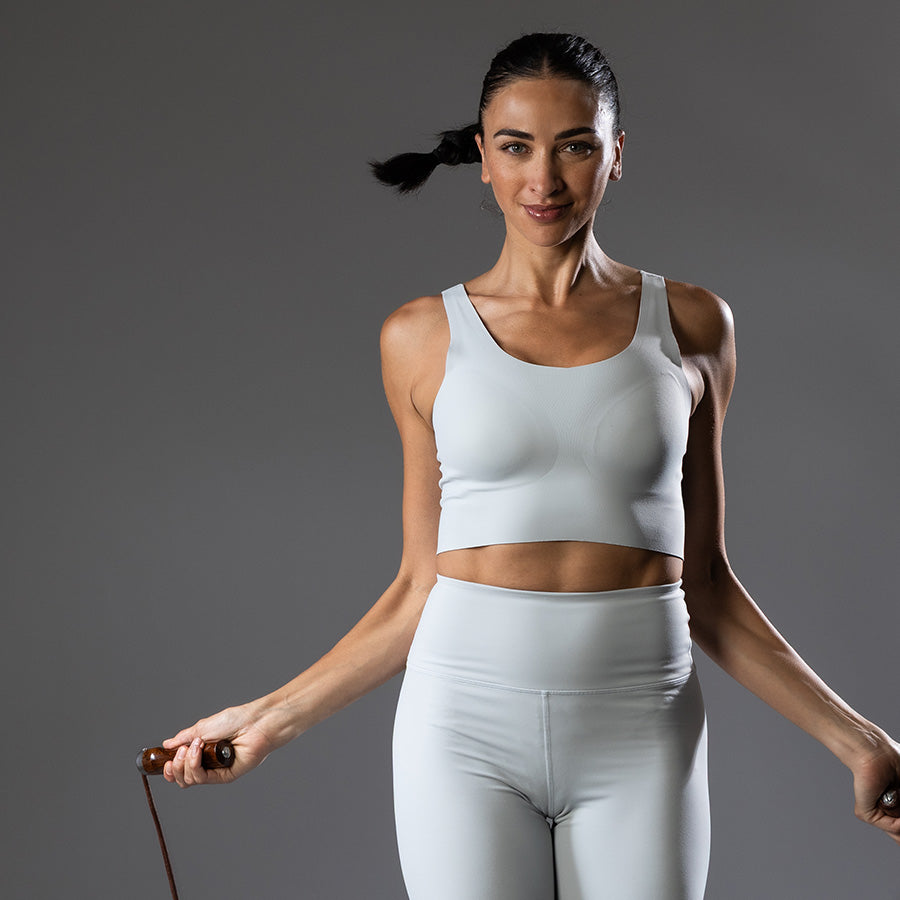 Woman in athletic wear holding a jump rope against a gray background
