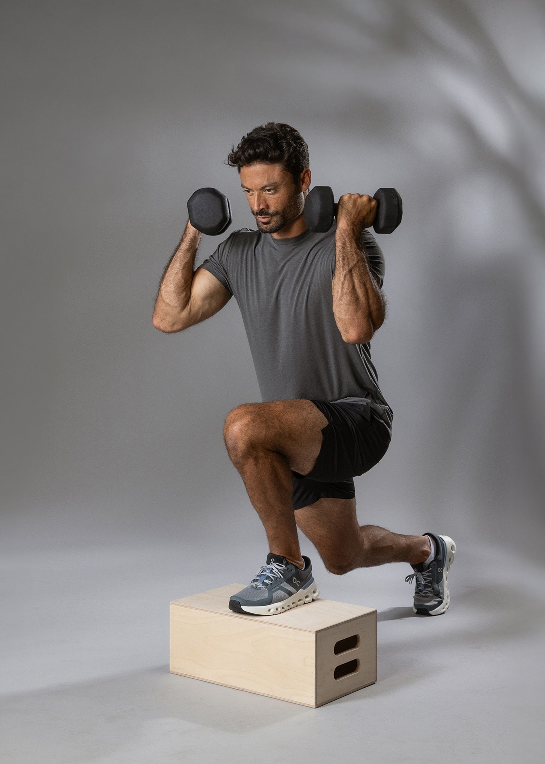 Man performing a squat exercise with dumbbells on a gray background