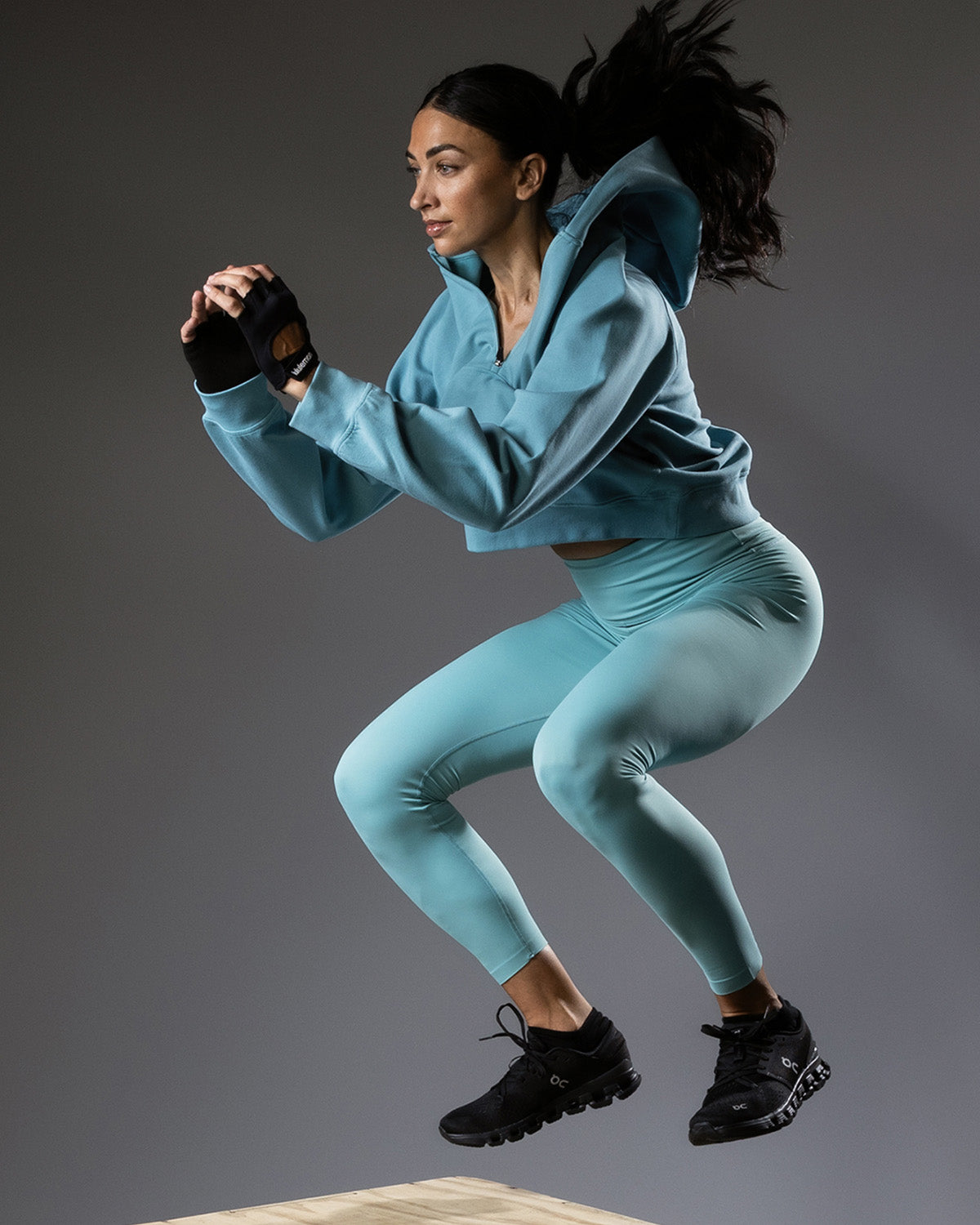 Woman in a blue athletic outfit performing a jump on a gray background