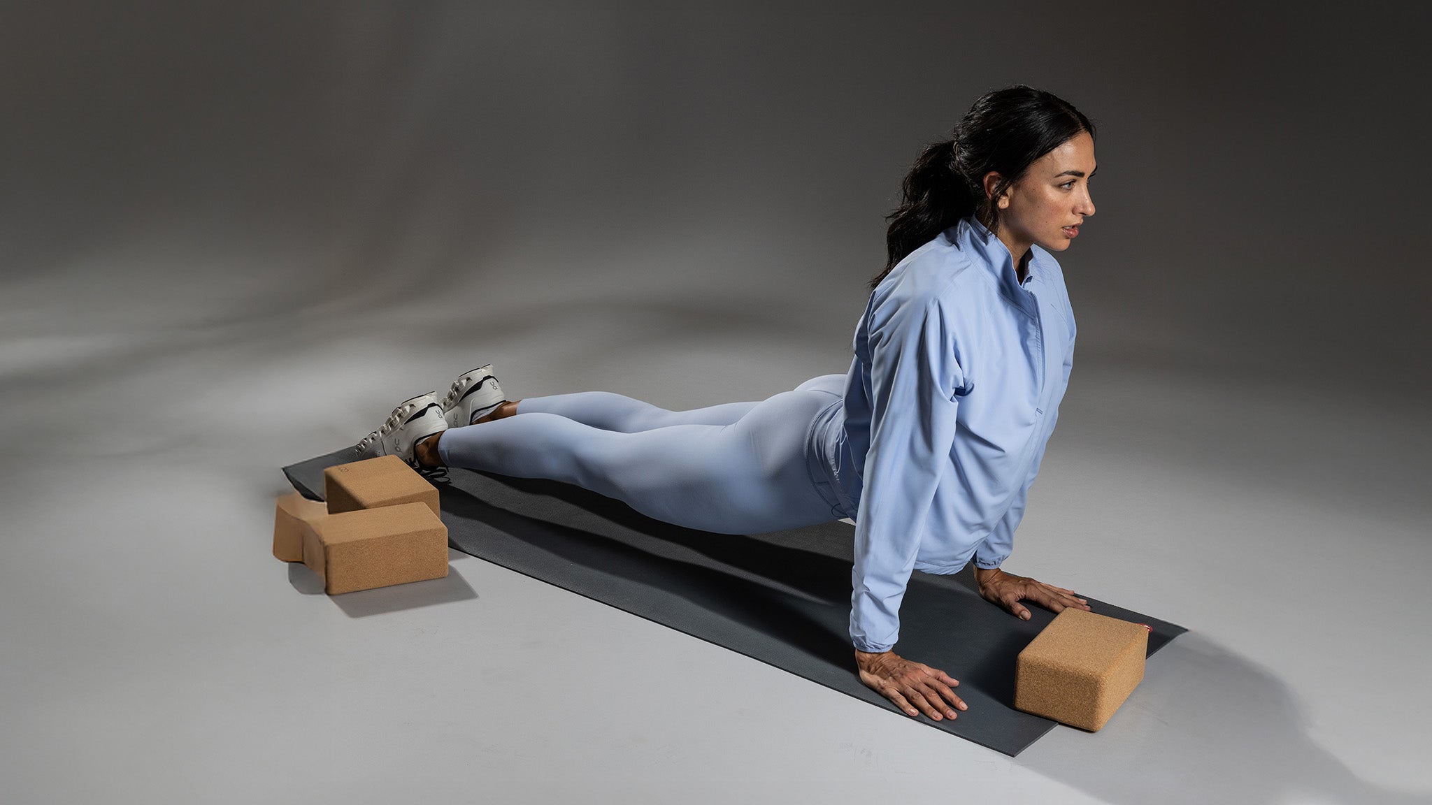 Woman performing a yoga pose on a mat with blocks on a gray background